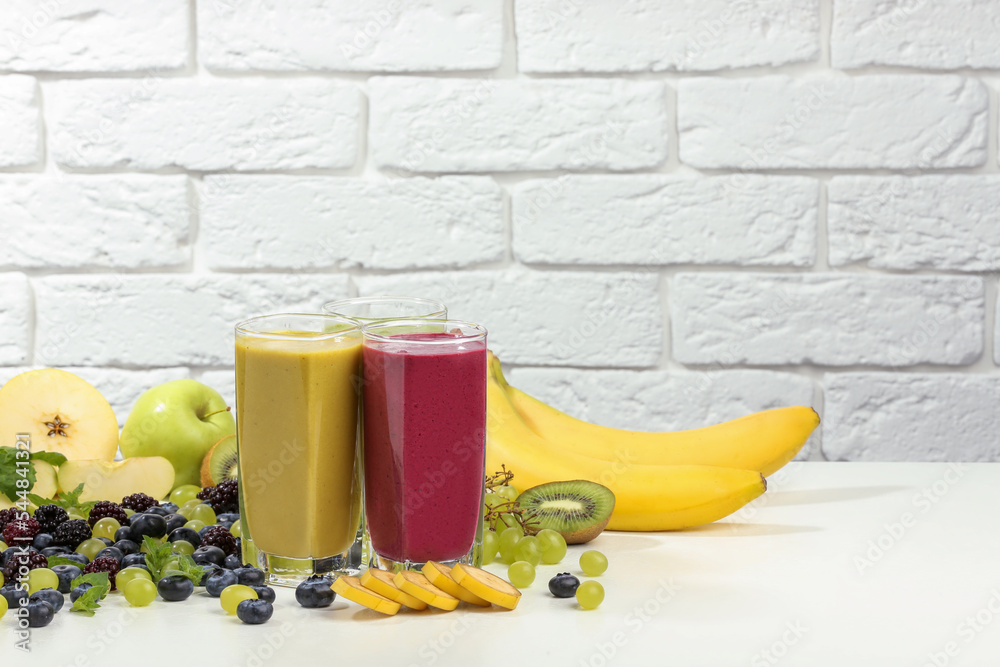 Fresh colorful fruit smoothies and ingredients on table against white brick wall. Space for text - obrazy, fototapety, plakaty 