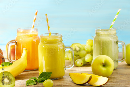 Mason jars of different tasty smoothies and fresh ingredients on wooden table
