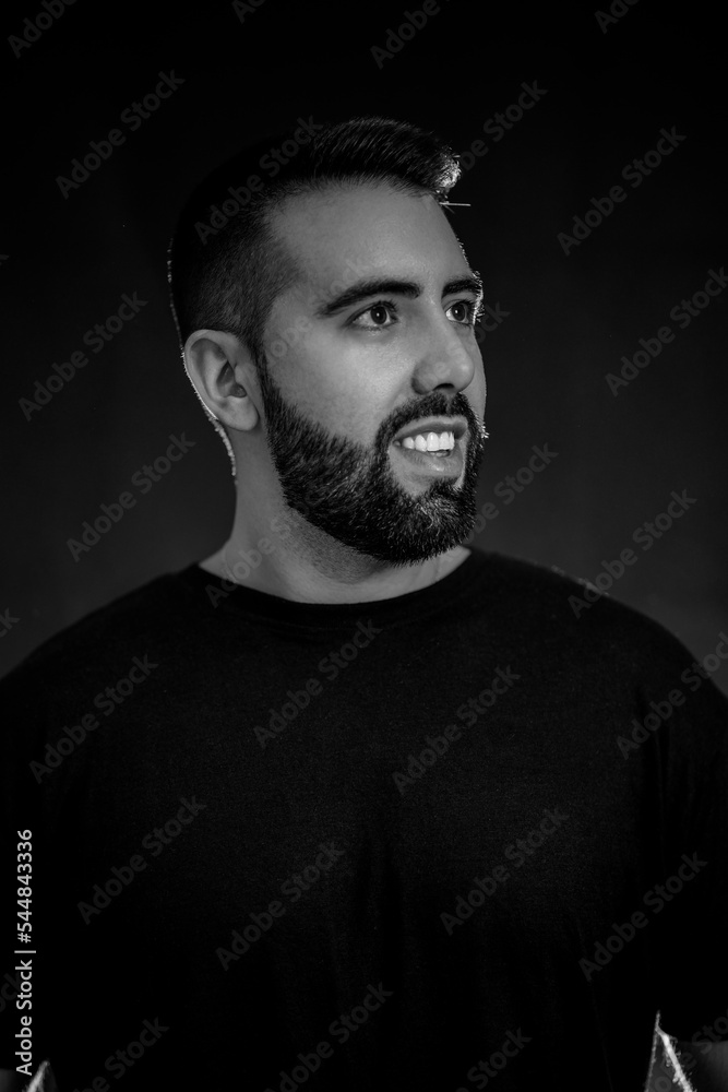 Fototapeta premium Portrait of a young man with beard in black and white on a black background with smoke.