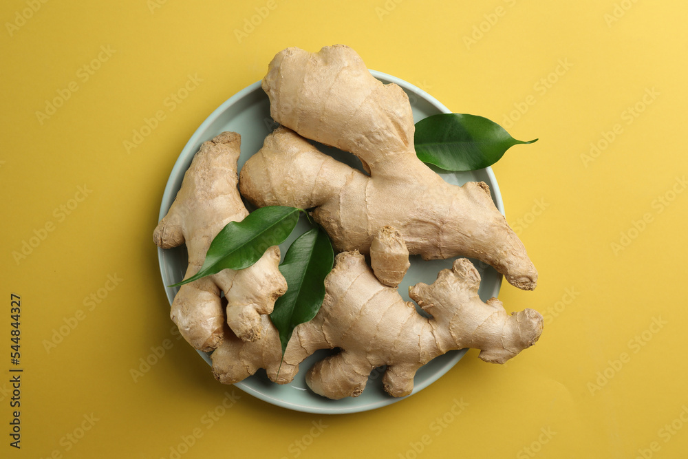 Fototapeta premium Fresh ginger with green leaves on pale light yellow background, top view