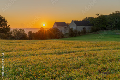 An autumn sunrise in Maastricht overlooking the meadows of the Sint Pieter hill with an historical farm Hoeve Zonneberg and a sun bringing its first rays of light over the landscape