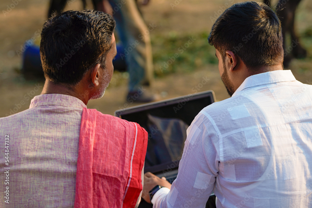 Young indian banker or agronomist showing some detail to farmer in laptop at home Young indian banker or agronomist showing some detail to farmer in laptop at home