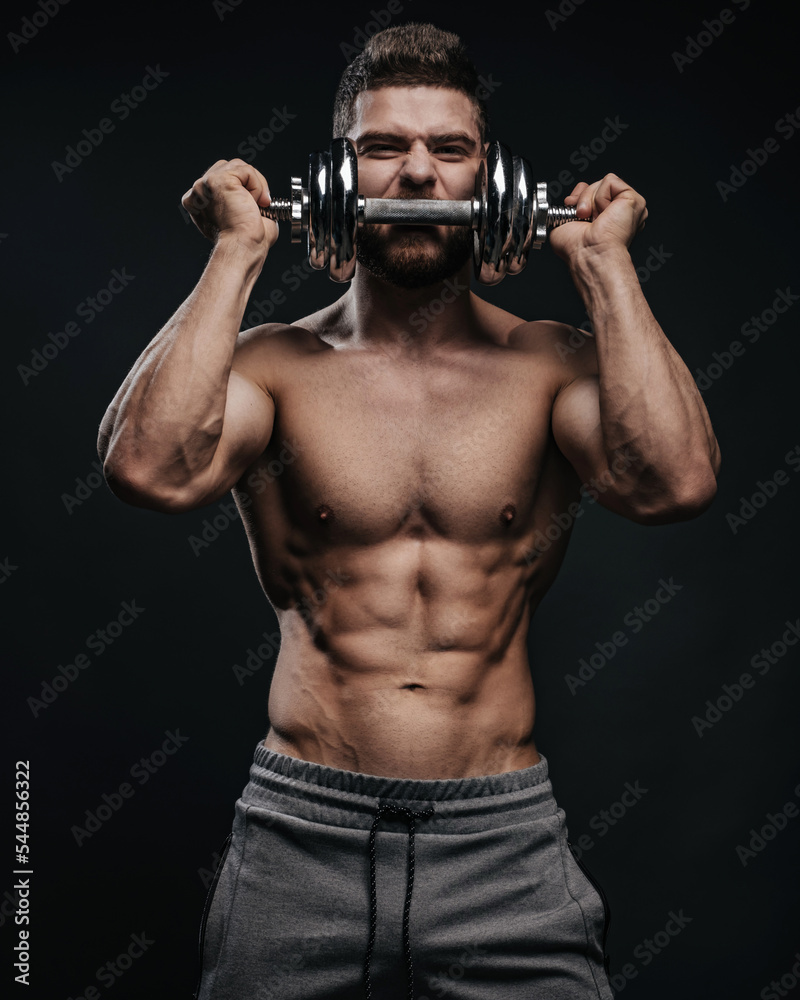 Muscular hunk with dumbbell posing in studio. Fitness male model holding gym equipment. Shirtless man at black background. Muscular hunk with dumbbell posing in studio. Fitness male model holding gym equipment. Shirtless man at black background.