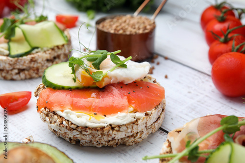 Crunchy buckwheat cakes with salmon, poached egg and microgreens on white wooden table, closeup