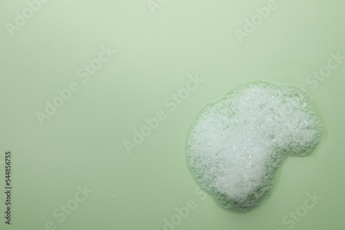 Drop of fluffy soap foam on green background, top view. Space for text