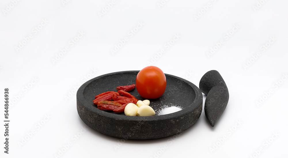 Red Chilies, Garlics, Tomato, and Salt on stone ware, ingredients for making traditional Indonesian Sambal Tomat or Spicy Tomato Sauce. Isolated on white background. Side view. Red Chilies, Garlics, Tomato, and Salt on stone ware, ingredients for making traditional Indonesian Sambal Tomat or Spicy Tomato Sauce. Isolated on white background. Side view.