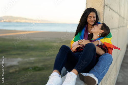 Happy lesbian young couple embraces and holds a rainbow flag. LGBT community