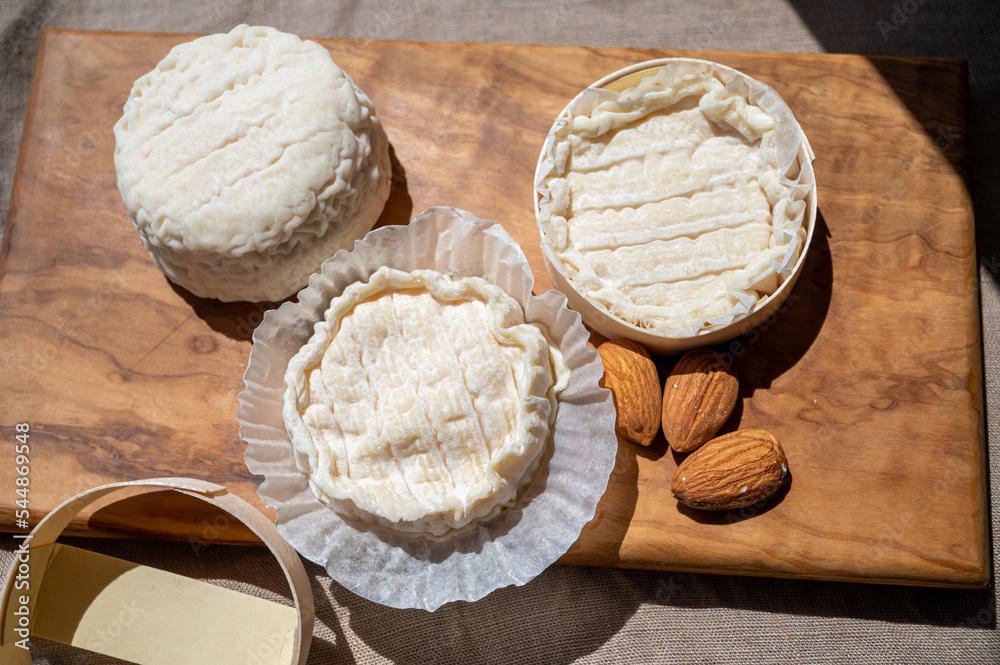 French cheeses Rocamadour and Saint-Marcellin served on olive tree wooden plank with almonds
