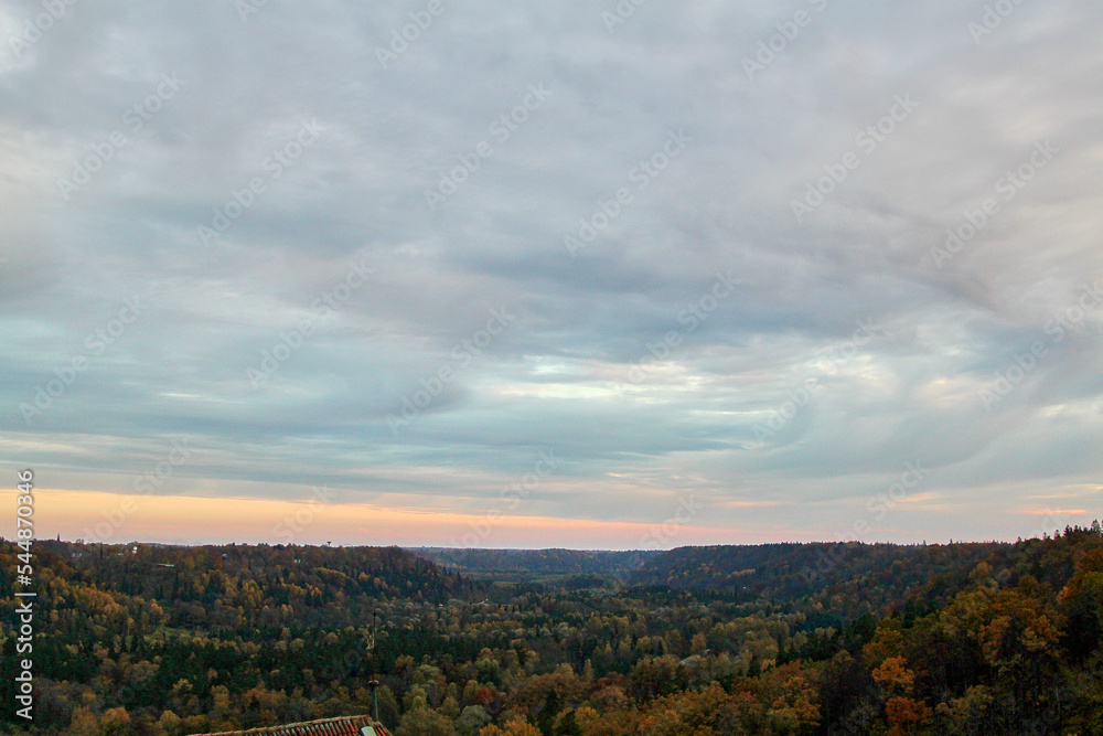 A beautiful view on colourful autumn forest and cloudy sky with slight evening fog. Selective focus