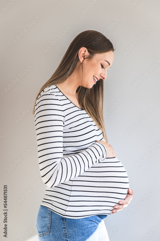 Portrait of a smiling pregnant woman against a white wall looking belly. Portrait of a smiling pregnant woman against a white wall looking belly.