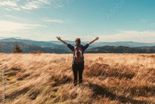 Girl with a backpack and outstretched arms enjoys the autumn mood view of the mountains