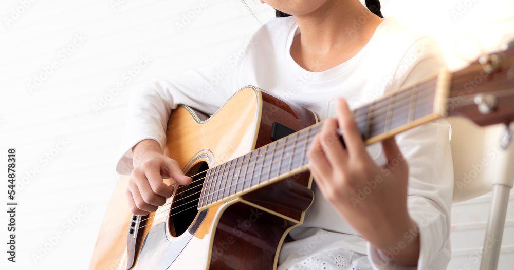 Talented female musician playing acoustic guitar on white background. Young asian guitarist put fingers on fingerboard of string instrument play fingerpicking melody. Child have fun learning as hobby.