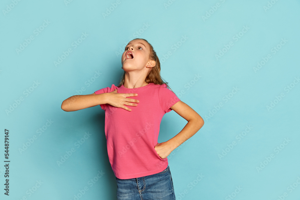 Portrait of little beautiful girl, child in pink T-shirt posing, loudly singing isolated over blue studio background Portrait of little beautiful girl, child in pink T-shirt posing, loudly singing isolated over blue studio background