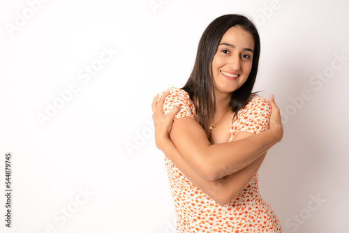 Young beautiful brunette woman wearing casual dress standing over white background Hugging oneself happy and positive, smiling confident. Self love and self care photo