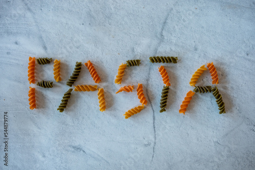 Word pasta spelled out in fuselli pasta that is tricolor and uncooked. photo