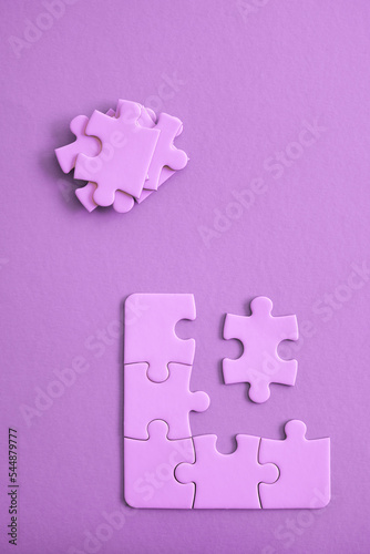 Purple jigsaw puzzle pieces on purple backgroun with pieces piled and ready to be fit.