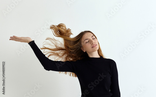 Fotografiet a beautiful woman tosses her long well-groomed hair standing on a light backgrou