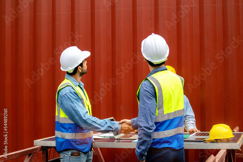Smart technicians in safety helmets and uniforms with having handshaking and looking upward, collaboration concept.