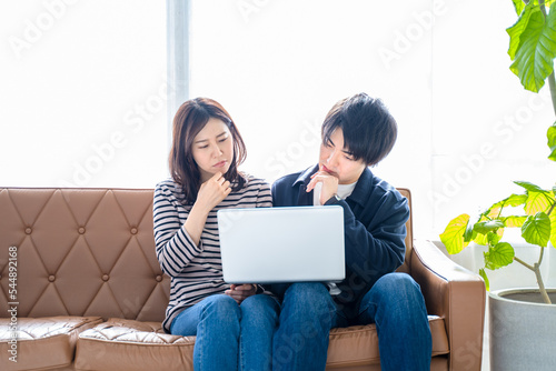 カップル夫婦-リビングのソファに座りパソコン作業で困る男女2人