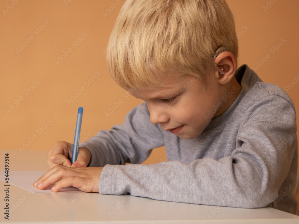 Little boy with hearing aid write book indoors Little boy with hearing aid write book indoors