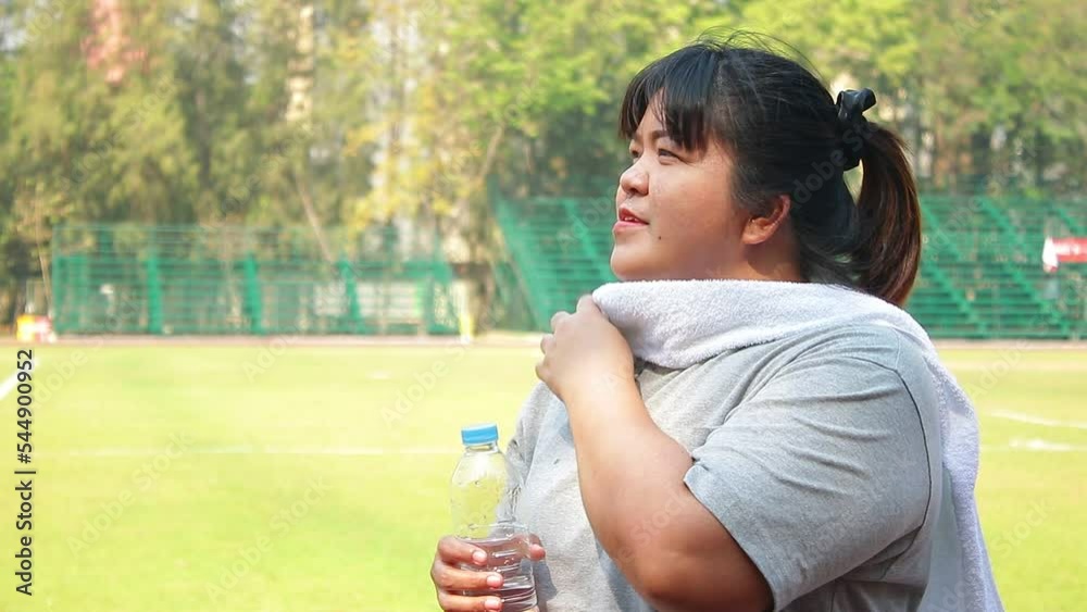 Fat Asian woman drinks water after finishing outdoor exercise. Concept of sports for health. weight loss Fat Asian woman drinks water after finishing outdoor exercise. Concept of sports for health. weight loss