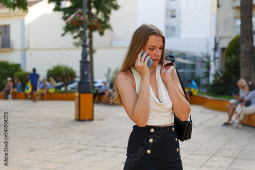 A young stylish woman communicates on a smartphone on a city street
