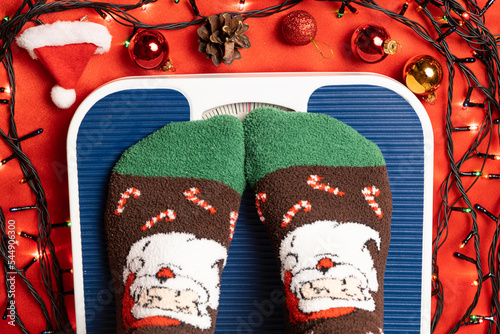 A woman in Christmas socks stands on the scales, weighs herself after gluttony during the holidays photo