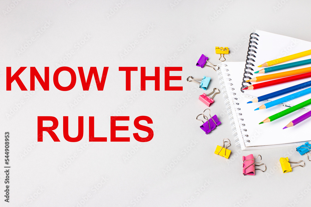 Notebooks, colored pencils and paper clips on a light gray table. The inscription KNOW THE RULES. Banner Notebooks, colored pencils and paper clips on a light gray table. The inscription KNOW THE RULES. Banner