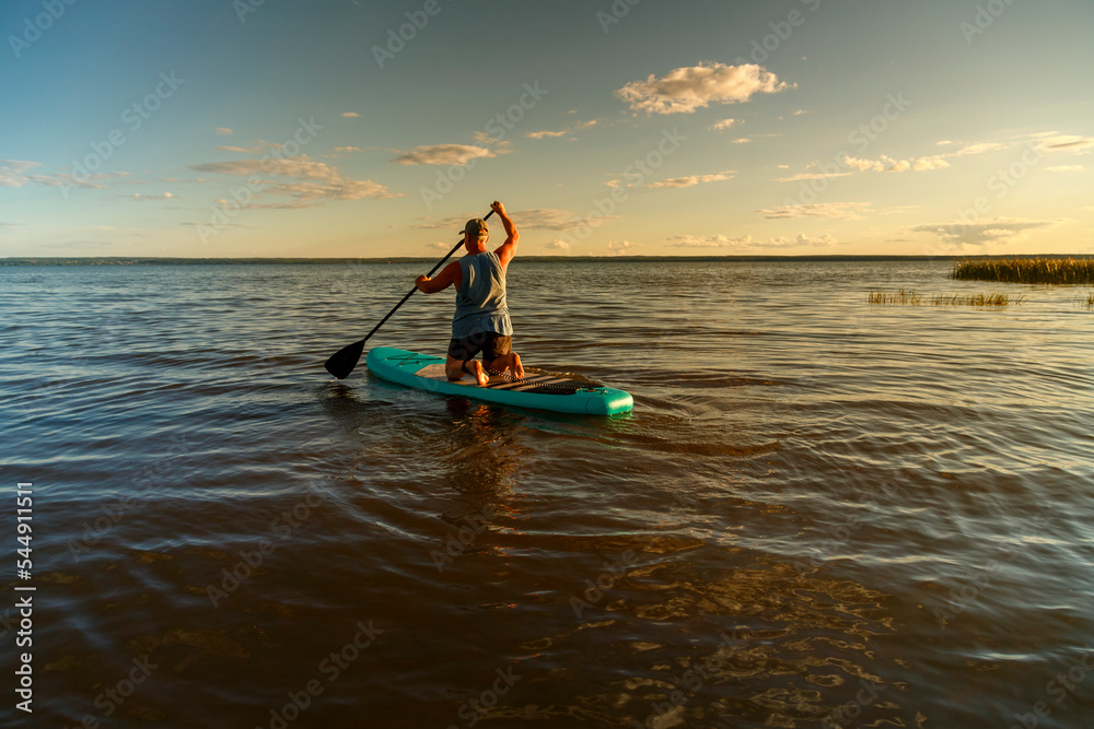 a man in shorts with a paddle on a sup board at sunset in the lake.