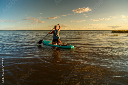 a man in shorts with a paddle on a sup board at sunset in the lake. © finist_4