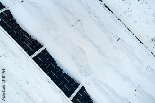 Aerial view of electrical power plant with solar panels covered with snow melting down in winter end for producing clean energy. Concept of low effectivity of renewable electricity in northern region