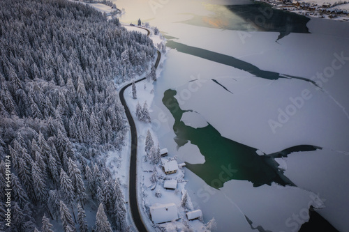 A top down, drone capture of Weissensee lake in Austrian Alps. Ice and green water. A small settlement at the shore. A bit of overcast. Serenity and peacefulness. January 2022 photo