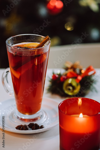 Traditional hot drink at Christmas time. Holiday concept. Close-up of candle and mulled red wine with aromatic spices and citrus fruits on white table on background decorated Xmas tree