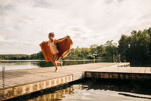Carefree girl running on jetty while holding towel during vacation photo