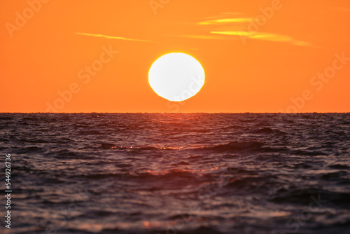 Fototapeta Naklejka Na Ścianę i Meble -  Ocean sunset. Big white sun on dramatic bright sky background, soft evening cloud over sea dark water