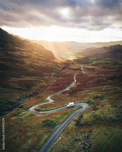 Fotografie Campervan travelling down winding road beneath dramatic sky