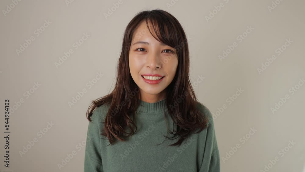 Young asian woman smiles. White wall. Dolly in.