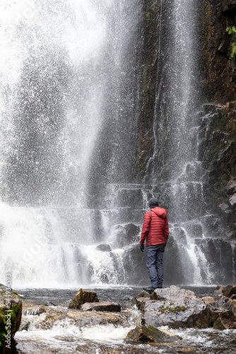 Man in front of a waterfall. Hiking in the Scottish Highlands, Red Down Jacket/coat. UK Hiking, The great outdoors, tourism