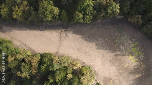 Dried up river bed with remains of dirty water in puddles, located in the forest area, aerial above view.
