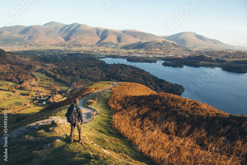 Leinwand Poster Hiker standing on Catbells looking out over Derwent Water at sunrise