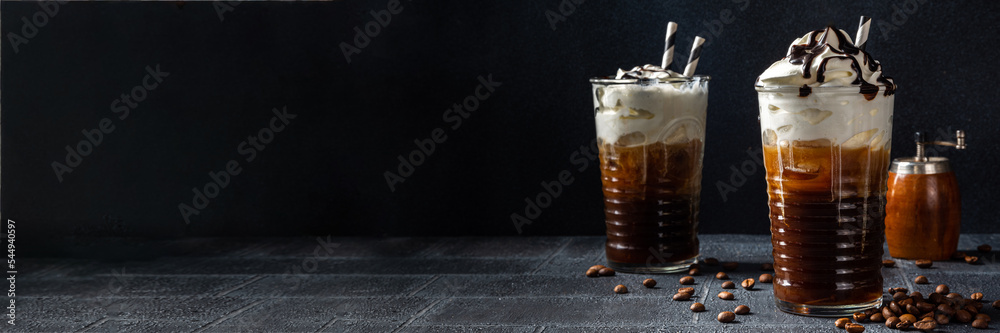 Cold coffee drink frappe (frappuccino), with whipped cream and chocolate syrup, with straws, coffee beans on a dark gray stone table, copy space  - obrazy, fototapety, plakaty 