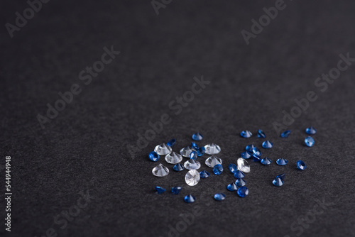 White and blue small calibrated size sapphires on black textured paper background. Natural genuine small precious leucosapphires and blue colored gem settings from Sri-Lanka. For jewelry making.