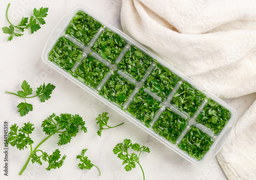 Frozen herbs for cooking. Fresh organic parsley and parsley ice cubes on a marble background. The concept of frozen food. Selective focus, top view and copy space