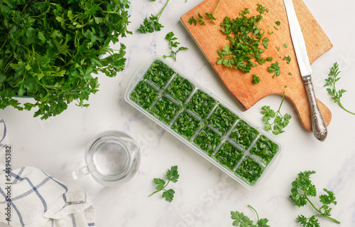 Frozen herbs for cooking. Fresh organic parsley and parsley ice cubes on a marble background. The concept of frozen food. Selective focus, top view and copy space