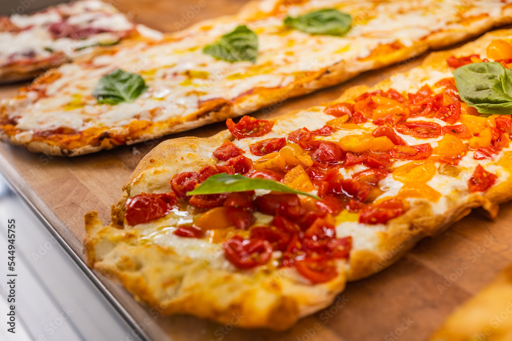 Pinse Romane con mozzarella, pomodori gialli e rossi e basilico fresco esposte in una vetrina di una rosticceria Pinse Romane con mozzarella, pomodori gialli e rossi e basilico fresco esposte in una vetrina di una rosticceria