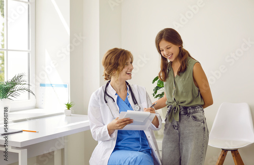 Doctor and child patient laugh at something funny while reading good results of health diagnostic. Friendly smiling pediatrician or general practitioner with stethoscope shows clipboard to happy girl