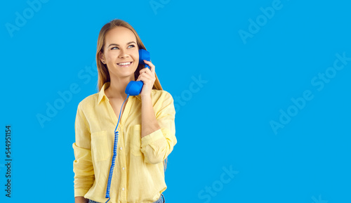 Smiling young woman on blue studio background talk on landline telephone. Happy millennial girl have pleasant call with customer service on corded phone. Helpline support. Copy space. photo