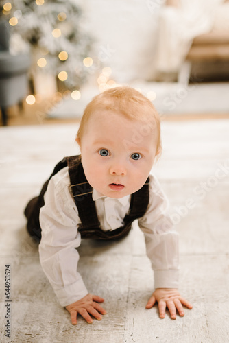 Little smiling and surprised baby boy crawling near Christmas tree. Christmas gifts, presents for New Year. Child looking magic boxes at home. Beautiful living room interior with winter decor. Closeup