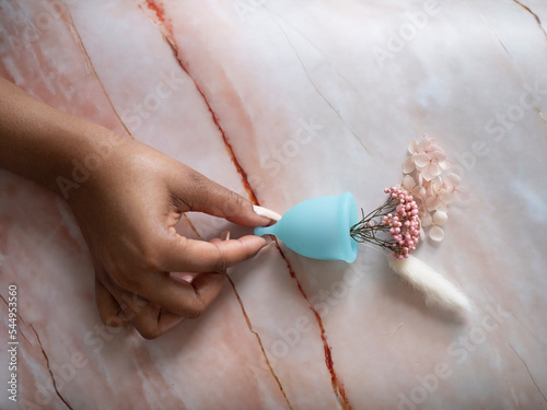 Woman's hand holding menstrual cup with flowers against marble surface photo