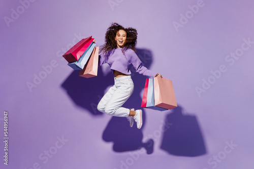 Full body exultant excited happy young woman wear pullover hold in hand paper package bags after shopping jump high isolated on plain pastel light purple background. Black Friday sale buy day concept. photo
